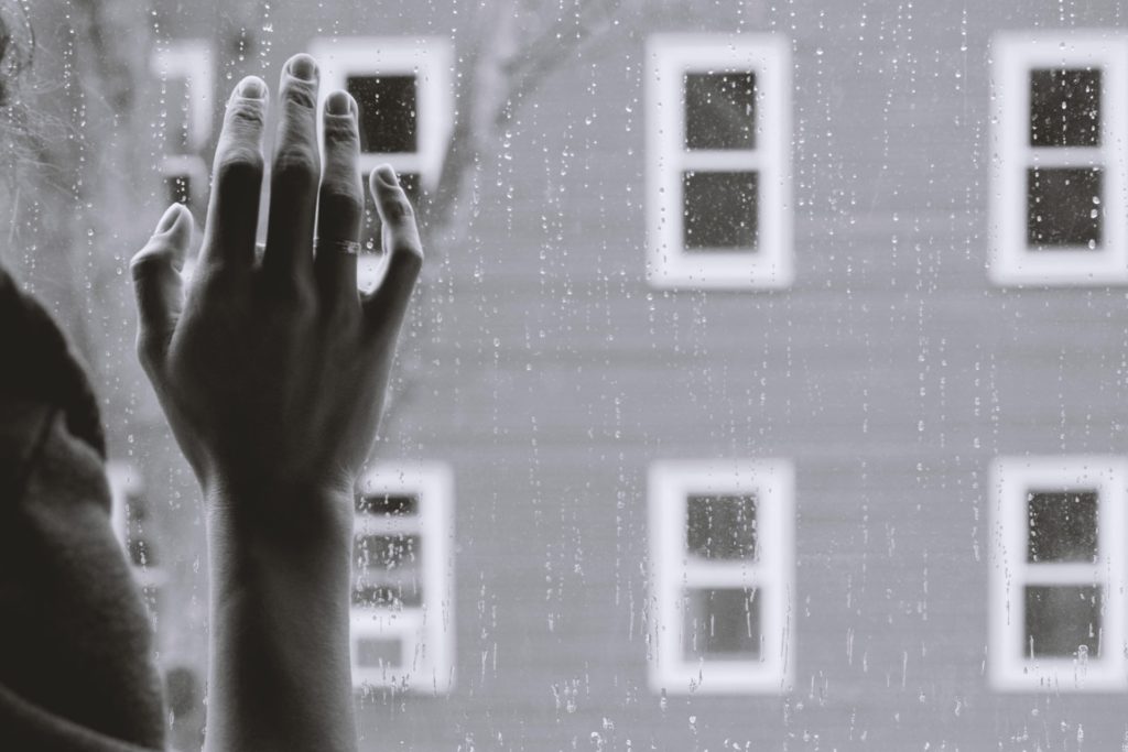 main posée sur une vitre avec vue sur un temps pluvieux